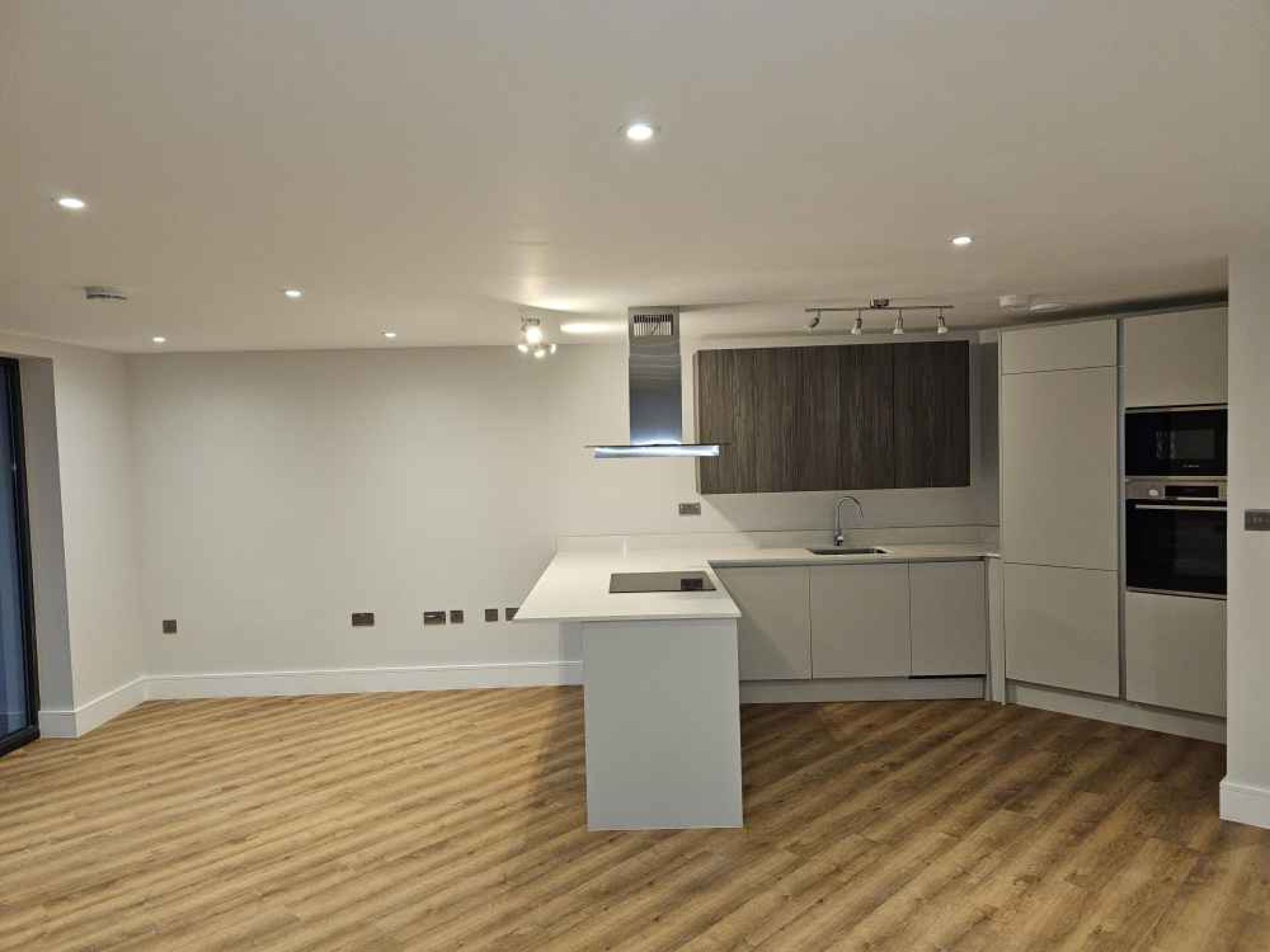 View of completed kitchen area in pegs lane flat. Wooden floor, white walls and oven.