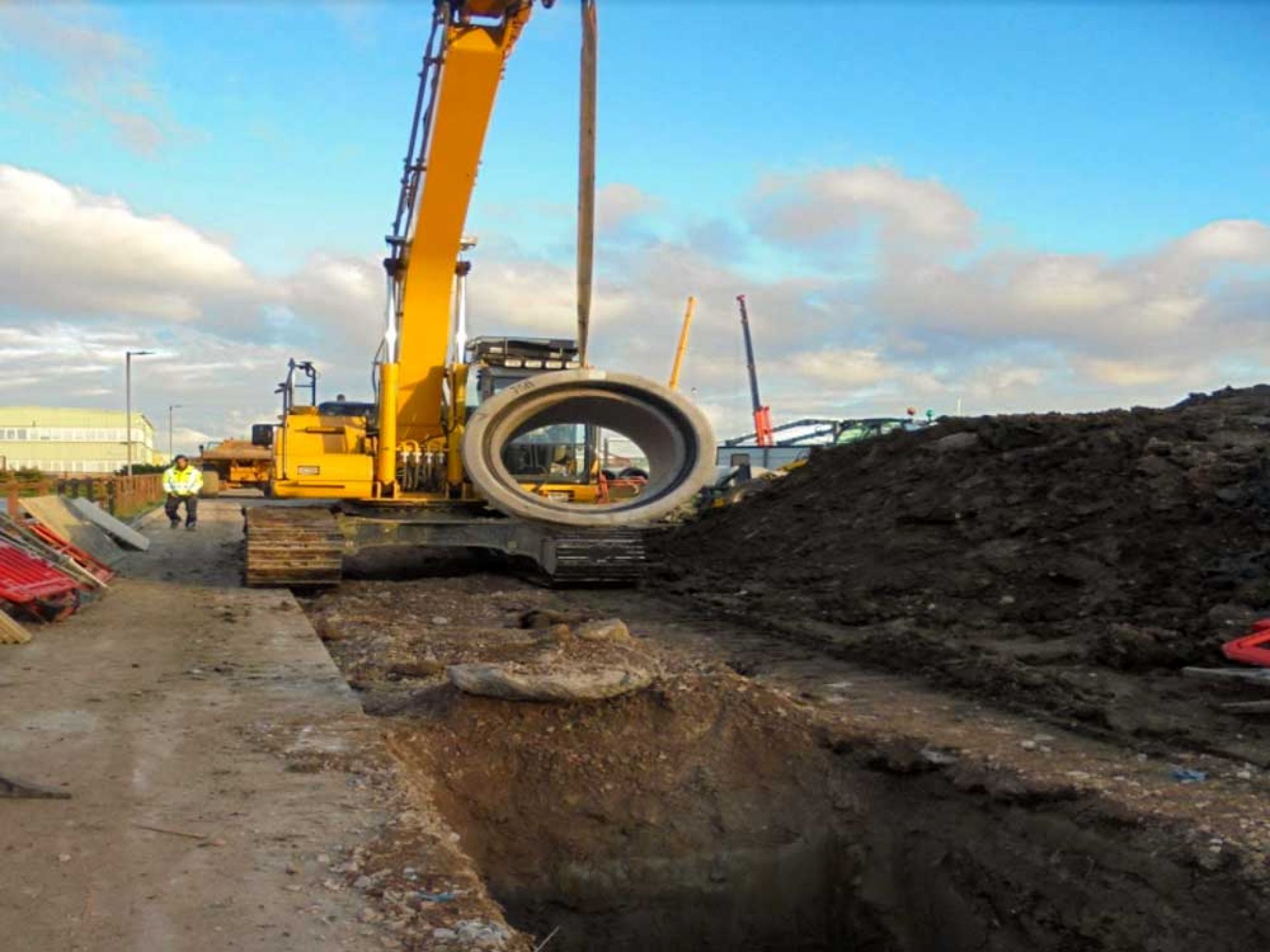 Large construction machine lowering circular concrete into the ground.