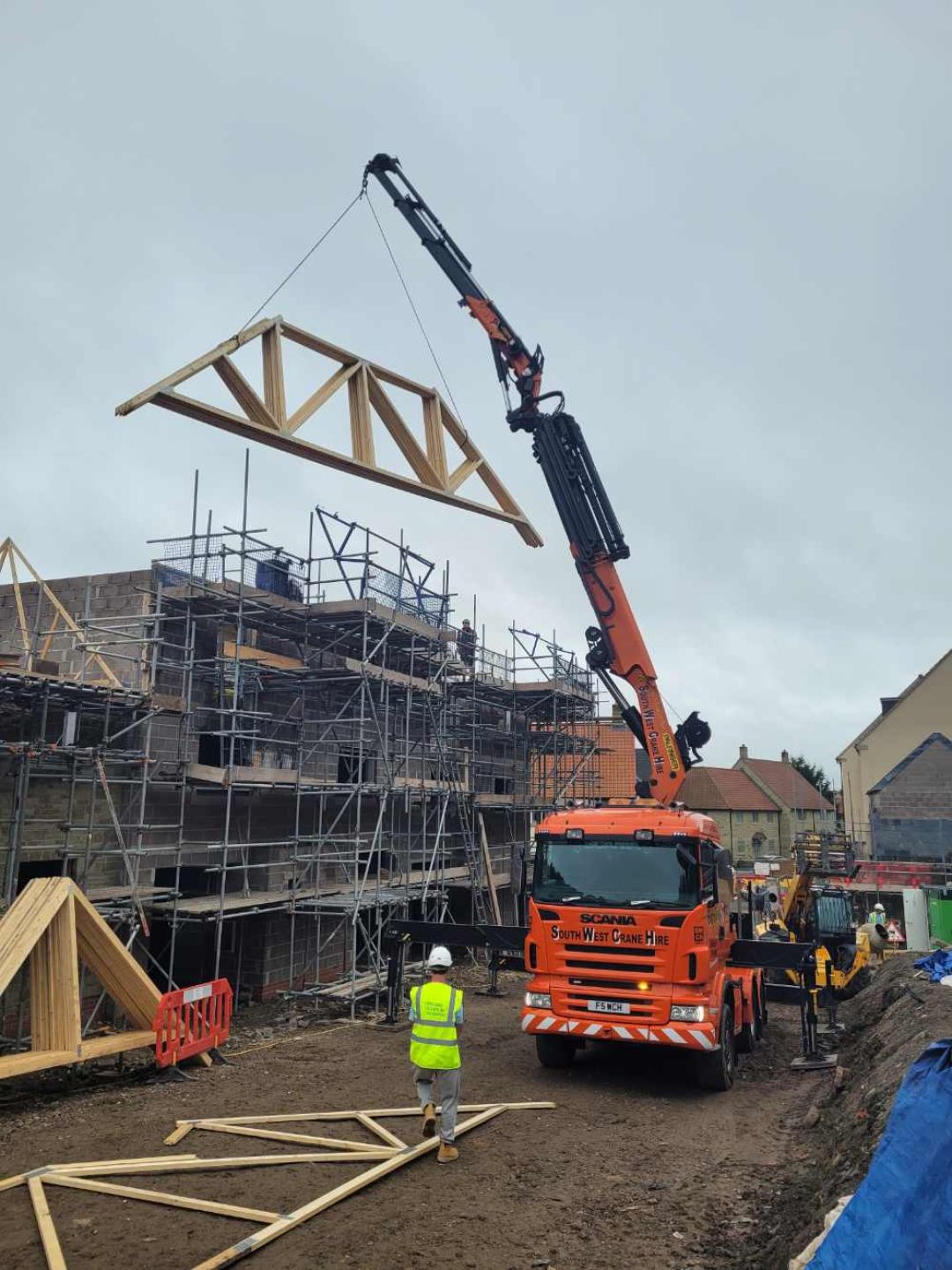 Excavator with a wooden roof truss being fitted to townhouse.