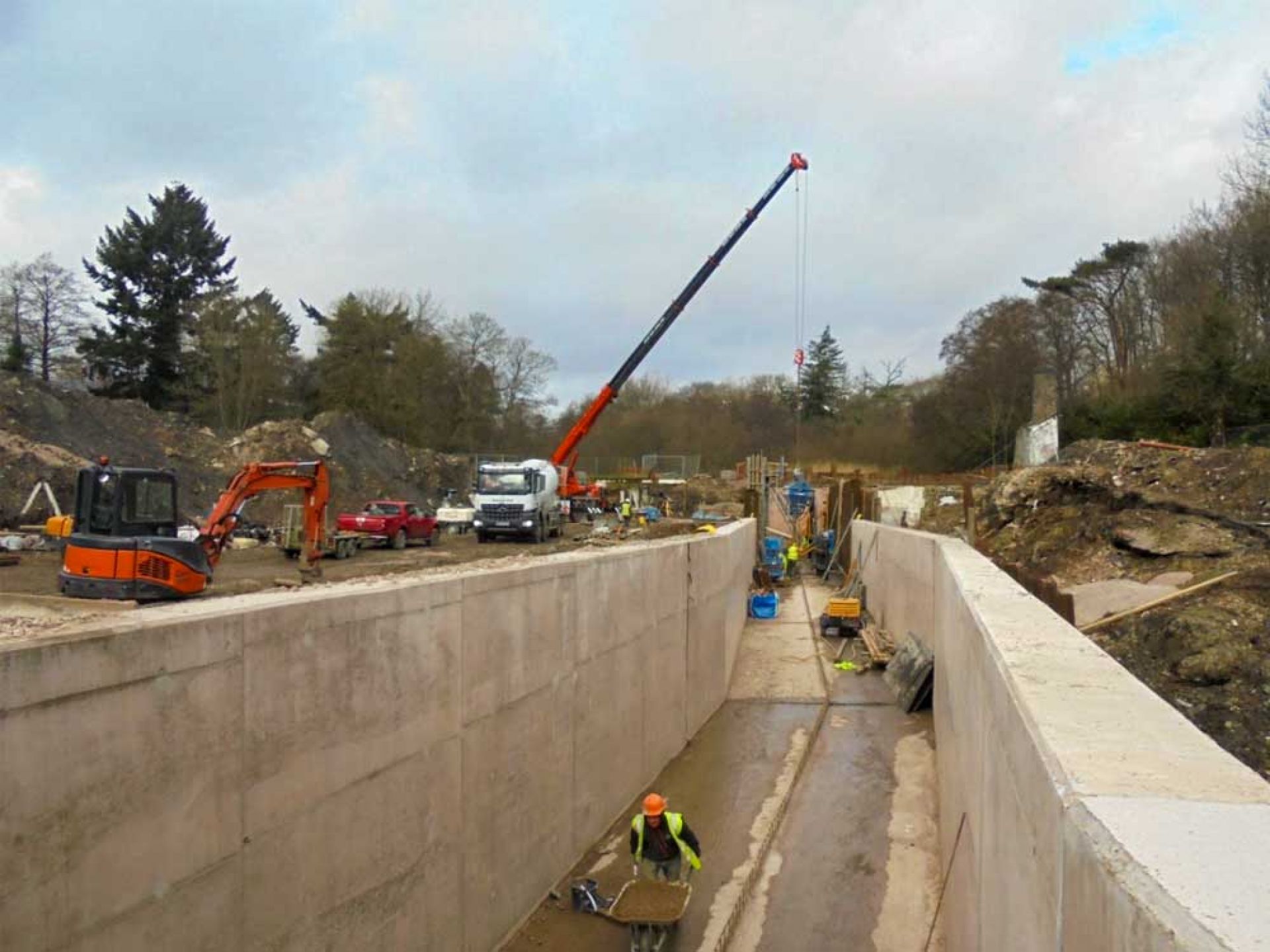 Construction men and machinery working on deep concrete flood channel.