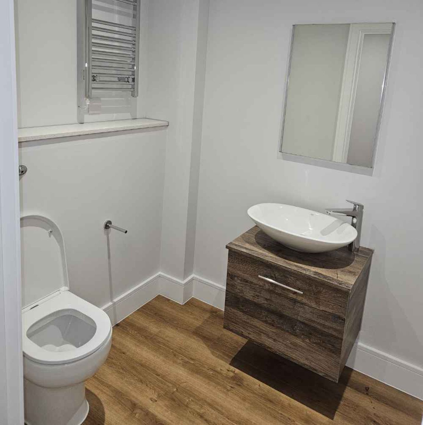 Completed toilet with basin area with wooden storage underneath.